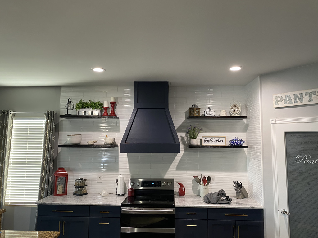 Finished kitchen with dark custom cabinetry, a custom range hood, and floating shelves