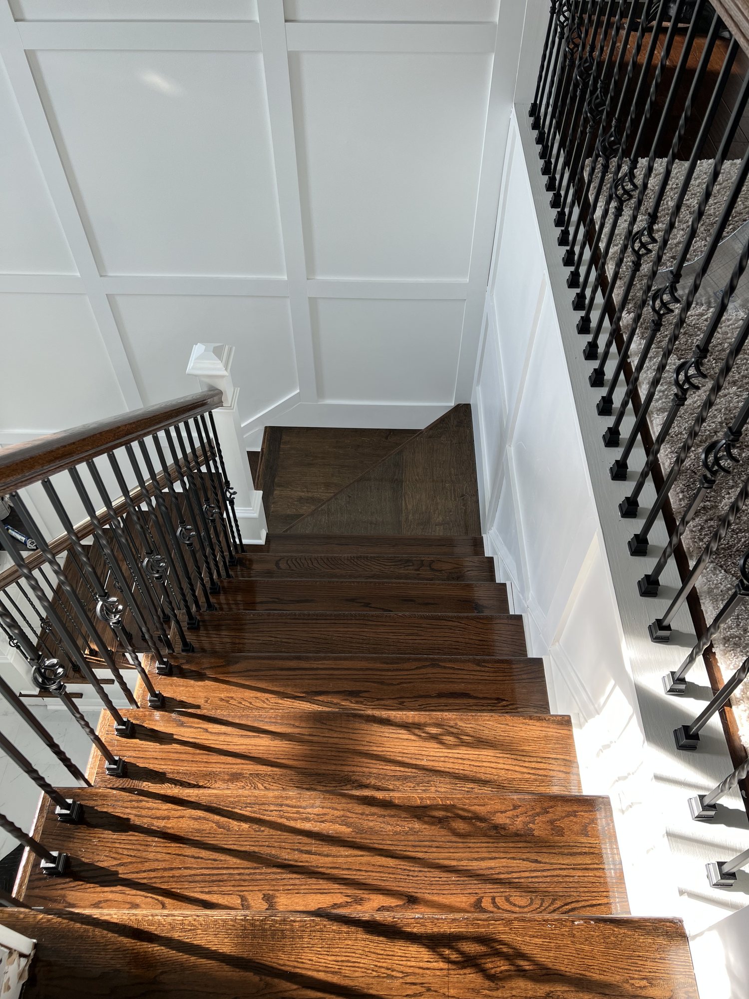 Finished custom oak staircase with iron balusters and paneled stairwell walls
